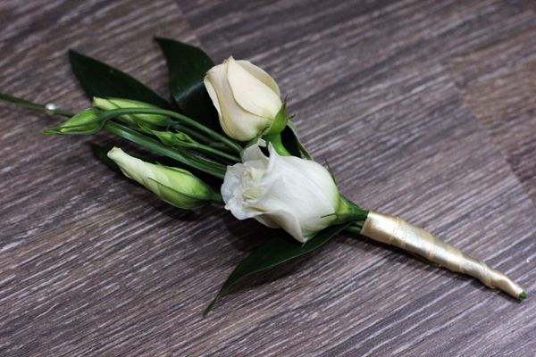 Бутоньерка из белых роз и зеленых листьев котинуса, украшенная белой бусиной, завязанная бежевой атласной лентой, на столе - фото 2506177 «ФлораДон» - оформление цветами 