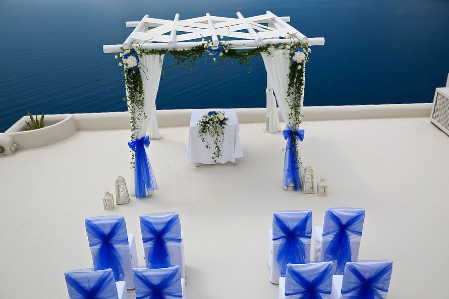 Квадратная арка- шатер, облаченная в белые ткани с синими лентами и нежными цветами  - фото 2329462 Exclusivaweddings - организация свадьбы на Санторини