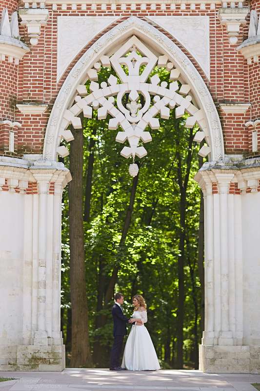 Жених и невеста, прислонившись друг к другу, стоят на фоне зелени и арки - фото 3005973 Юлия Segeln