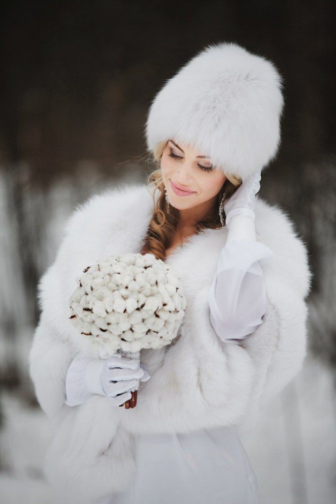 На голове невесты белая песцовая шапка, в ушах длинные серебристые серьги со стразами, на плечах белая пелерина из песцового меха - фото 2064886 White Fur - прокат меховых свадебных аксессуаров