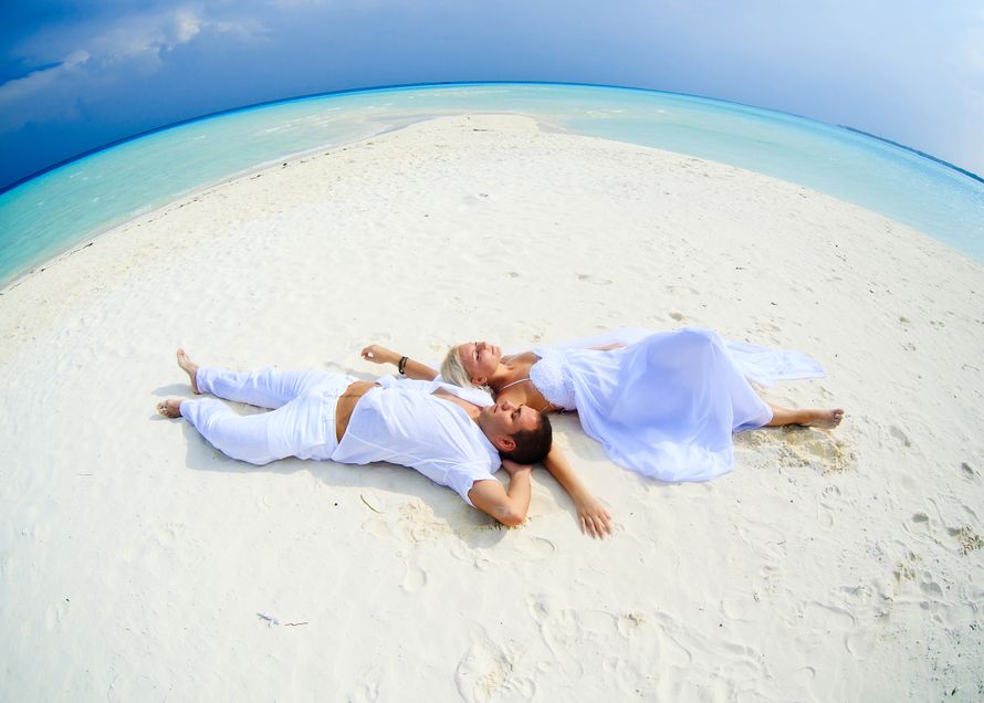 На пляже, лежат на спине жених и невеста раскинув руки, она в белом платье, он в белой рубашке и брюках - фото 3580955 Фотограф Анна Ахутина
