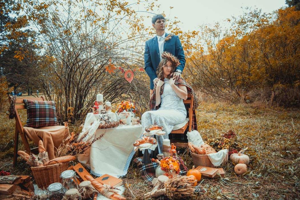 На фоне осенних деревьев жених и невеста сидят за столиком, укрытым белой скатертью,а рядом лежат баночки, тыквы, корзинки и - фото 3070155 Фотограф Анна Рагушкина