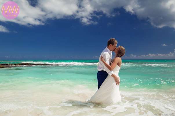 В волнах лазурного океана целуются молодожены, жених в серых брюках и белой рубашке обнимает невесту в белом открытом платье - фото 2369474 Mainland Travel Bureau - свадьба за границей