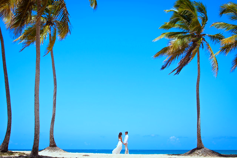 Жених с невестой идут по пляжу в белых одеждах, на фоне голубого небосвода и пальм - фото 2477429 Wedding in Dominicana - свадьбы в Доминикане  