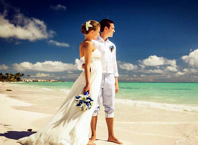 На побережье стоят влюбленные и смотрят вдаль, жених в белых брюках и рубашке, невеста в открытом белом платье держит в руке - фото 2477463 Wedding in Dominicana - свадьбы в Доминикане  