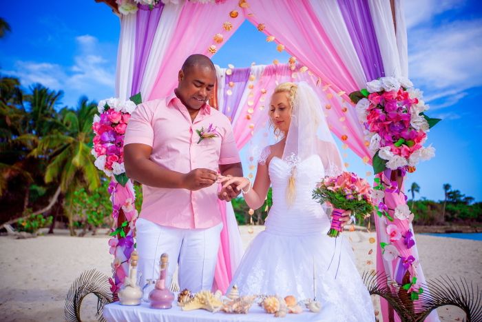 Возле свадебного шатра, украшенного в розовых и сиреневых тонах, жених в белых брюках и розовой рубашке одевает кольцо невесте в - фото 733169 Свадебное агентство "Свадьба-Недорого"