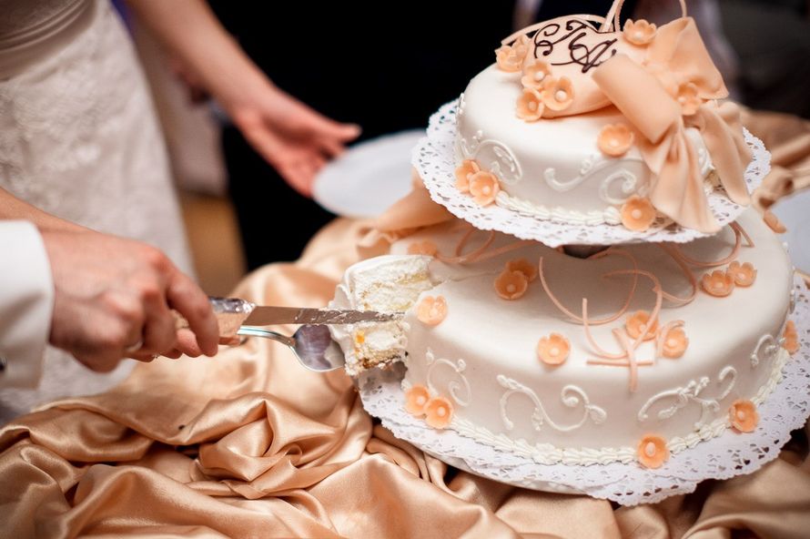 Невеста с женихом разрезают двухъярусный белый свадебный торт, украшенный оранжевыми цветочками, бантиком и сердечками. - фото 2633675 Ведущий Антон Богатый