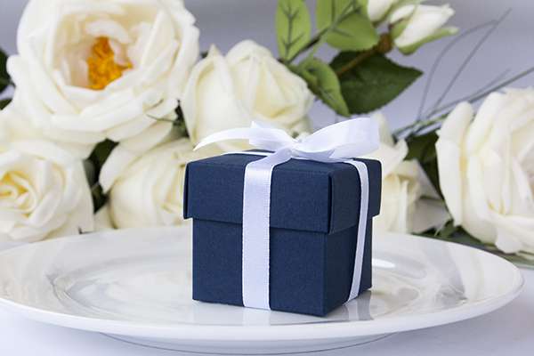 Синяя бонбоньерка с белой ленточкой на фоне столовых приборов. - фото 2747789 "Gold Day" - свадебные аксессуары