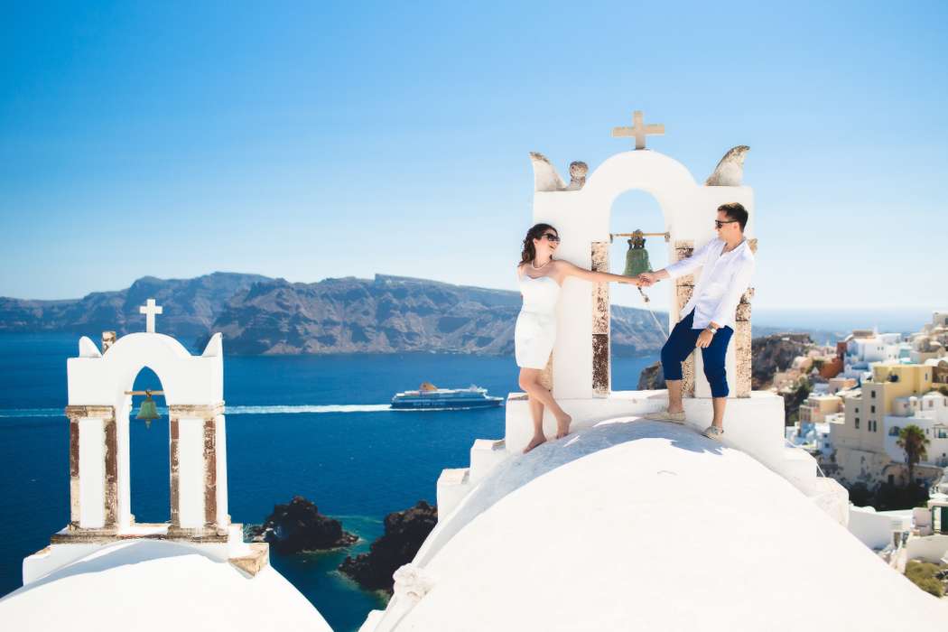 Жених и невеста, прислонившись друг к другу, стоят на белом здании на фоне моря  - фото 3470817 Santoweddings - свадьбы на Санторини