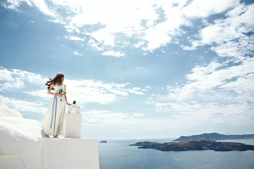 Невеста стоит на крыше белого здания и смотрит на море - фото 3470833 Santoweddings - свадьбы на Санторини
