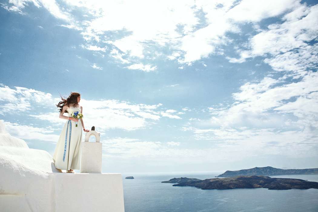 Невеста стоит на крыше белого здания и смотрит на море - фото 3470833 Santoweddings - свадьбы на Санторини