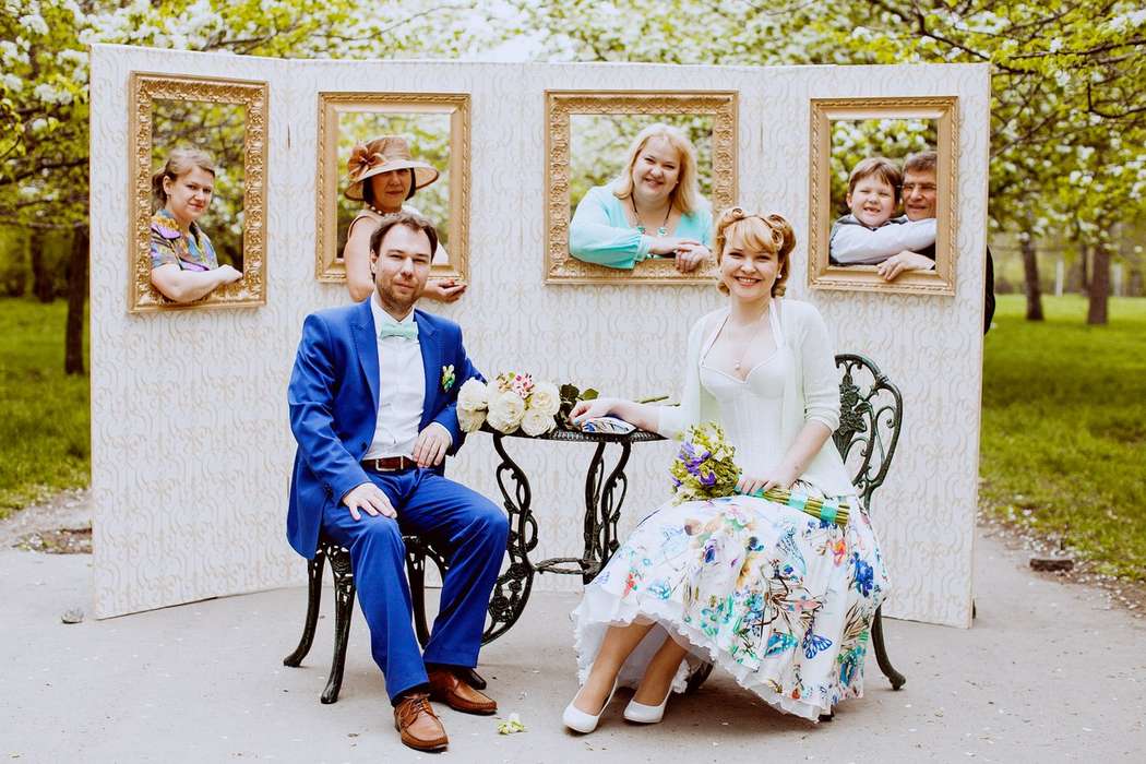 Гости выглядывают из окон белого пресс-вола, а жених и невеста сидят за маленьким столиком - фото 1068143 Angie