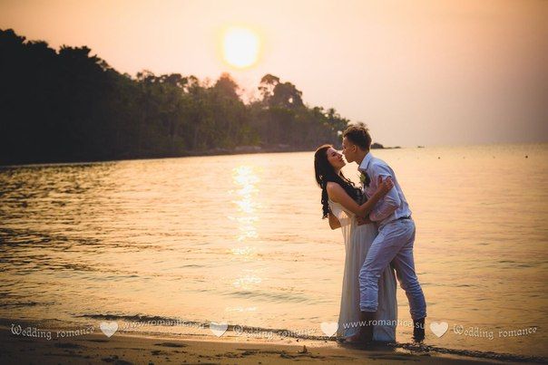 В лучах заката на тропическом пляже стоят влюбленные, жених в белых брюках и рубашке, придерживая за спину невесту в белом - фото 2832707 Romantica - свадебное агентство в Таиланде