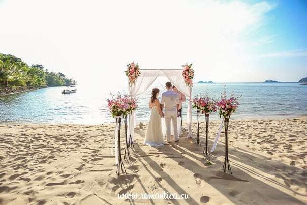 На песчаном пляже по дорожке к свадебному шатру, украшенному белой тканью и гирляндами цветов идут молодожены в белых одеждах, - фото 2832715 Romantica - свадебное агентство в Таиланде