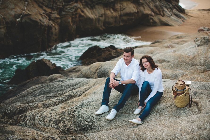На каменистом берегу сидит влюбленная пара, на них синие брюки и белые рубашки, рядом с ними корзина с продуктами для пикника, - фото 2274986 Фотограф Ксения Пардо
