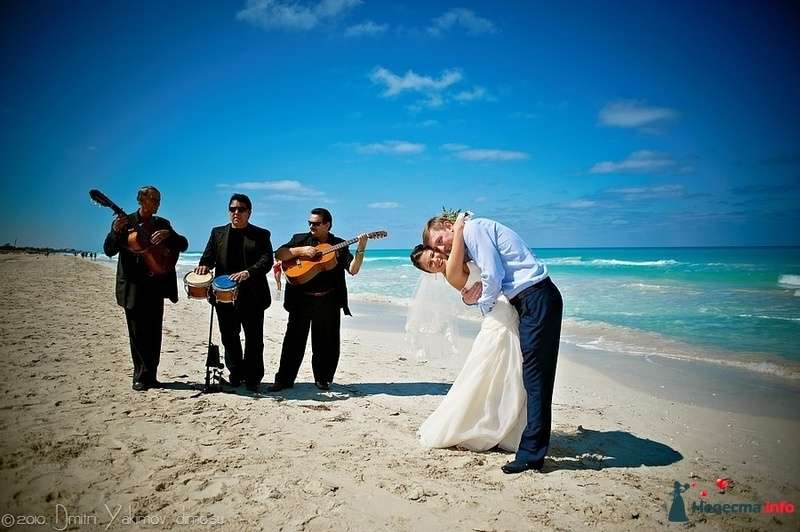 На песчаном пляже жених обнимает невесту в белоснежном платье за талию, наклонив ее назад, она нежно обнимает его за шею, позади - фото 151824 Софочка
